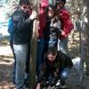 Group of people in jackets huddled around tree standing on small wooden platform. 