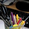 a variety of colorful pens in a cup resting in front of a computer keyboard