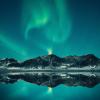 Green and blue Northern Lights shimmering above mountain and lake landscape