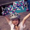 Young girl wearing helmet holding skateboard over her head 