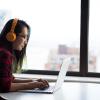 A girl wearing headphones sitting at a laptop near a window