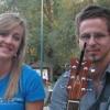 Young woman smiling seated on bench next to young man with guitar