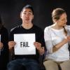 Three young people sitting holding signs. Two wearing black T-shirts hold up signs with "Fail" written on them. The third woman is wearing white holding a sign that says "Grace."