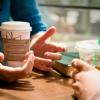 Closeup of two people's hands holding coffee tumblers on table