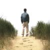 Back of young man staring off into the distance on beach with footprints in sand