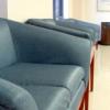 A gray leather couch sitting in a hallway with smooth concrete floors.