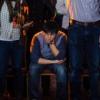 a sad-looking man sitting down in a crowd of standing people