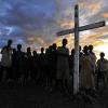 Wooden cross surrounded by group of children with sunset in the background